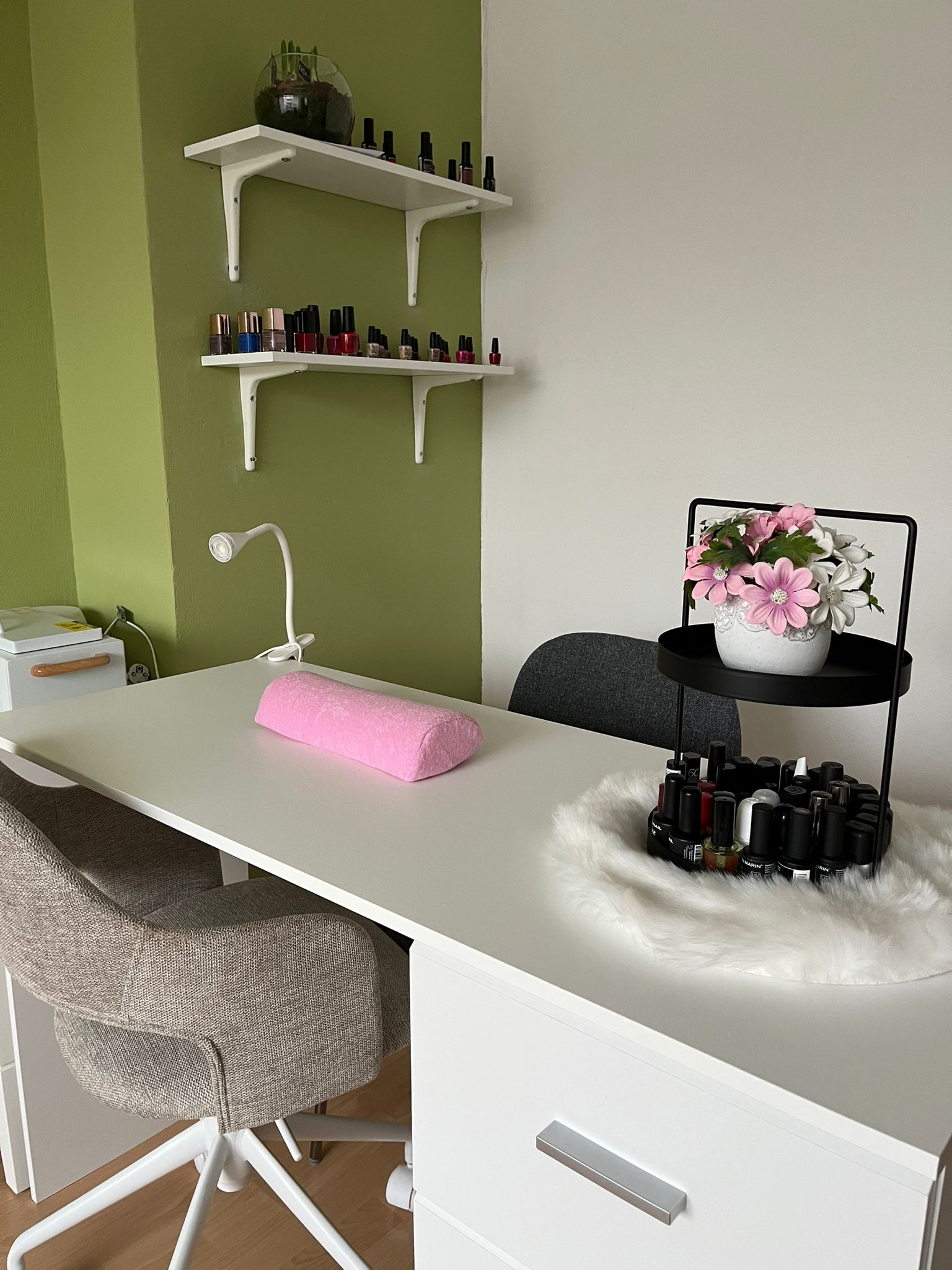 De nageltafel van Manu's Beauty Salon: roze handkussen, plankjes met nagellak en een groene wand