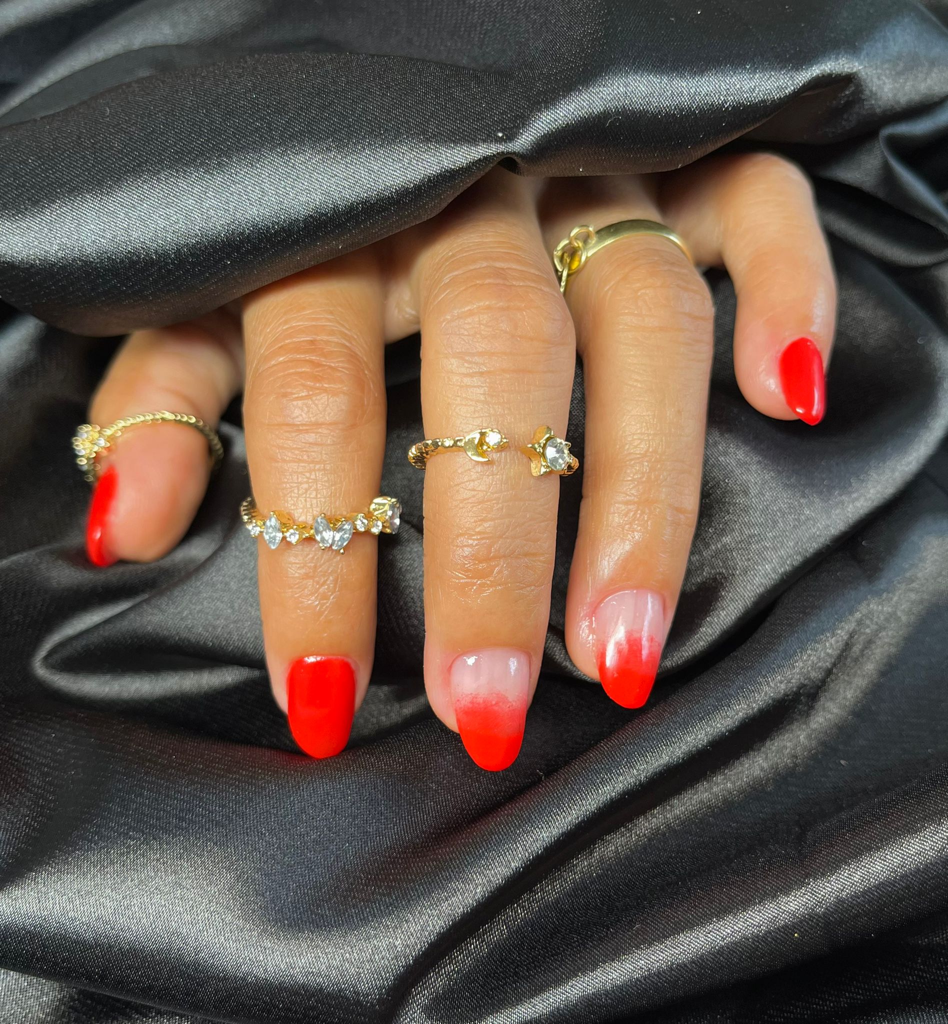 Rode ombre nagels met gouden ringen op zwart satijn